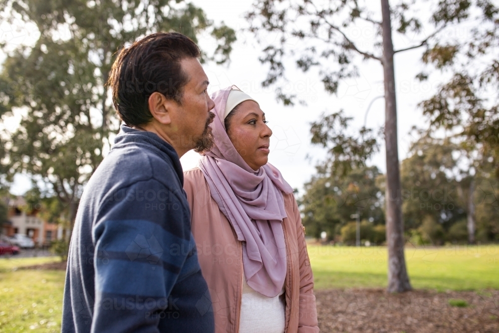 middle aged woman wearing pink hijab and middle aged man wearing blue sweater looking away - Australian Stock Image