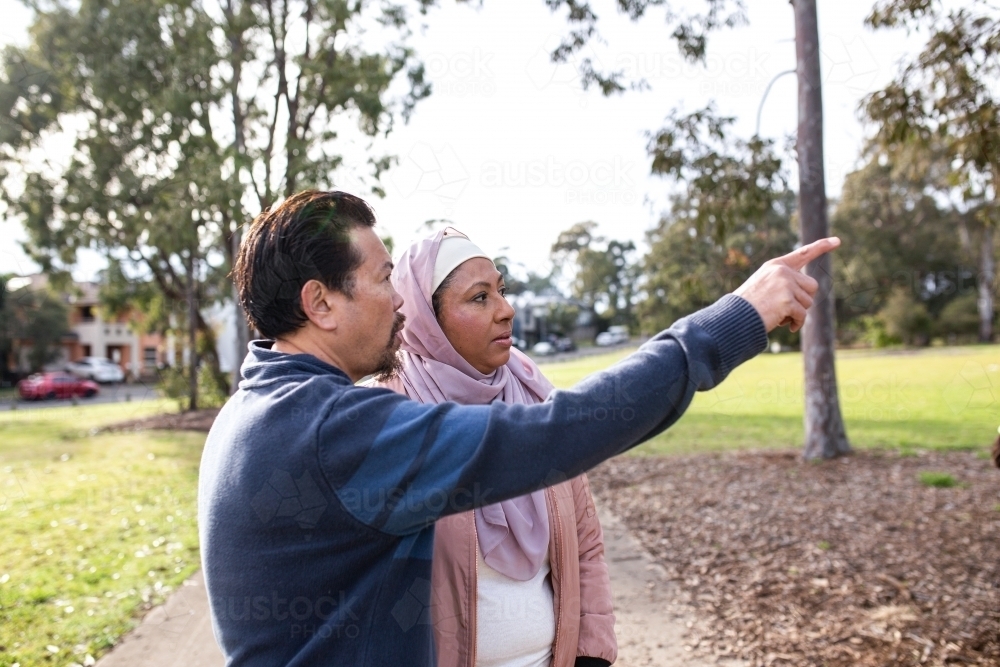 middle aged woman wearing pink hijab and middle aged man wearing blue sweater pointing - Australian Stock Image