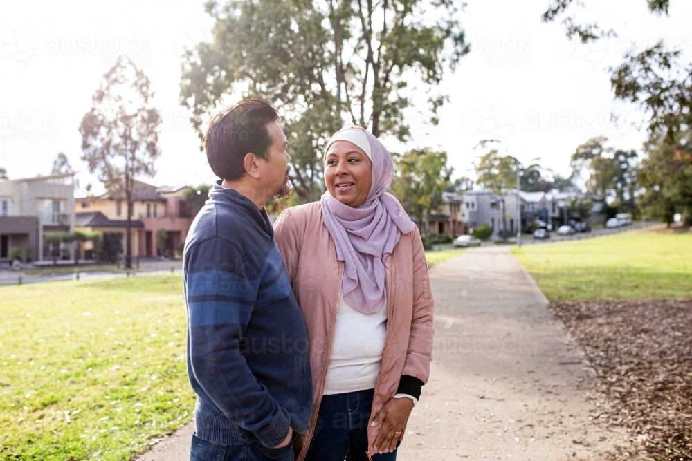 middle aged woman wearing pink hijab and smiling middle aged man looking at each other on a big lawn - Australian Stock Image