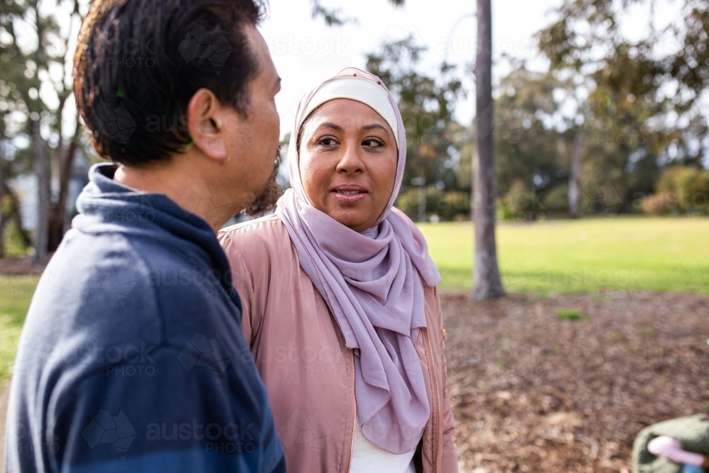 Middle aged woman wearing pink hijab looking at a middle aged man wearing blue sweater on a big lawn - Australian Stock Image