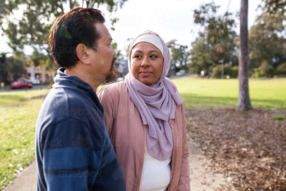 Middle aged woman wearing pink hijab looking at a middle aged man wearing blue sweater on a big lawn - Australian Stock Image