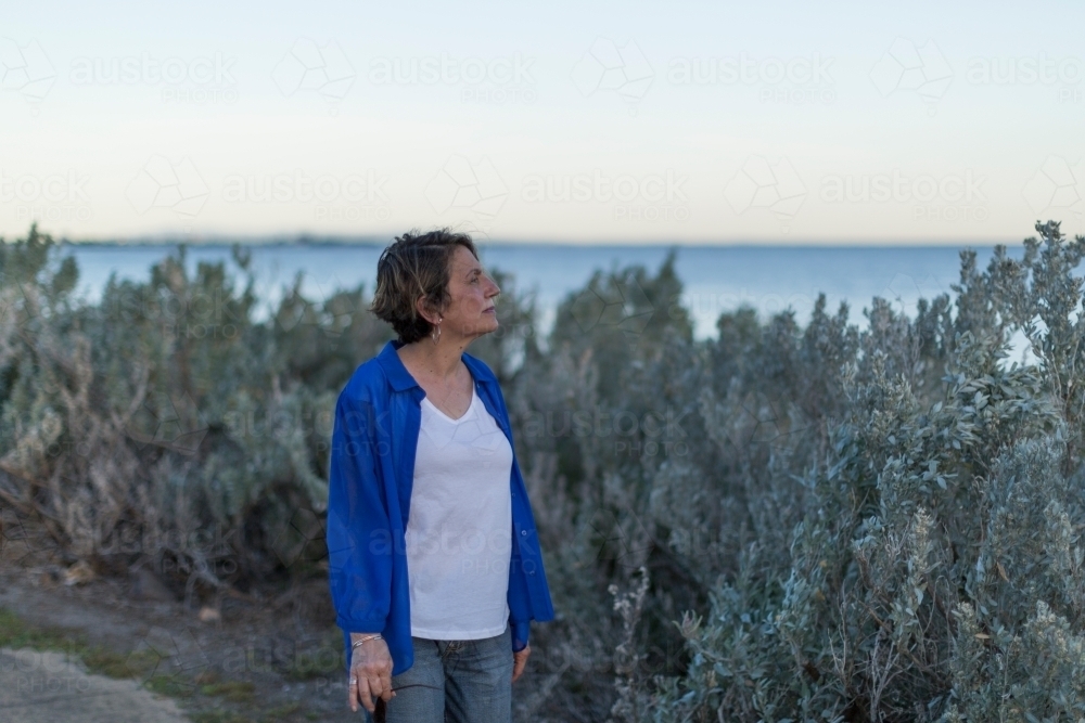 Middle eastern woman walking on shoreline at dusk - Australian Stock Image
