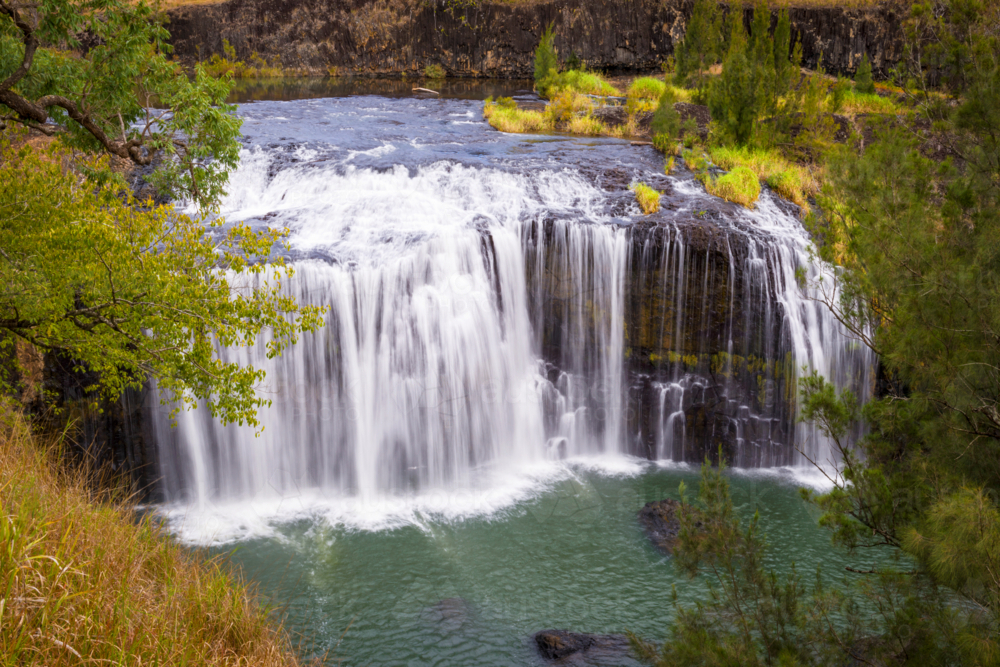 Millstream Falls cascading into a turquoise pool surrounded by lush greenery. - Australian Stock Image