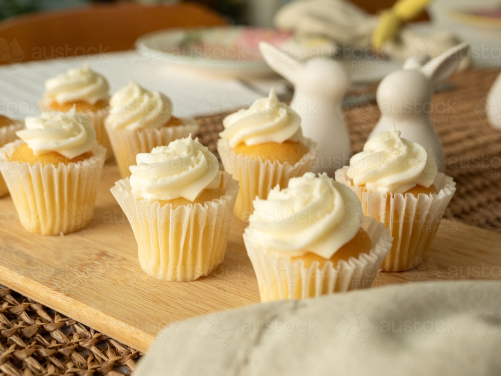 Mini cupcakes with white icing on wooden board with easter table decorations - Australian Stock Image