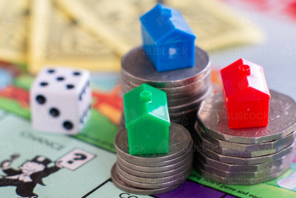 Miniature houses on stacks of coins on monopoly board - Australian Stock Image