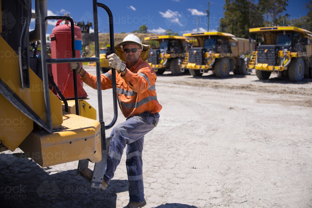 Mining operator man holding on the handrails while climbing up the dump truck - Australian Stock Image