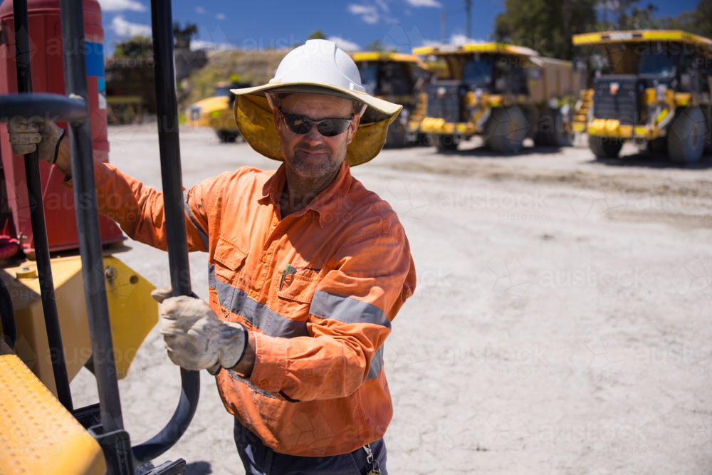 Mining operator man holding on the handrails while climbing up the dump truck - Australian Stock Image