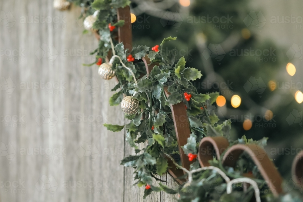 Mistletoe and delicate Christmas lights strewn along rustic wooden seat. Golden bokeh in background. - Australian Stock Image