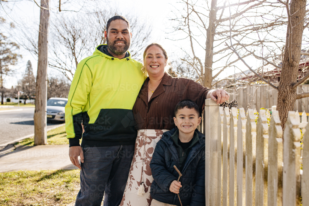 Mixed ethnicity couple with their younger son standing beside picket fence outdoors - Australian Stock Image