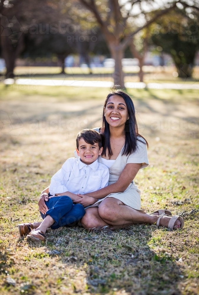 Mixed race aboriginal and caucasian boy sitting on grass with aboriginal mother - Australian Stock Image