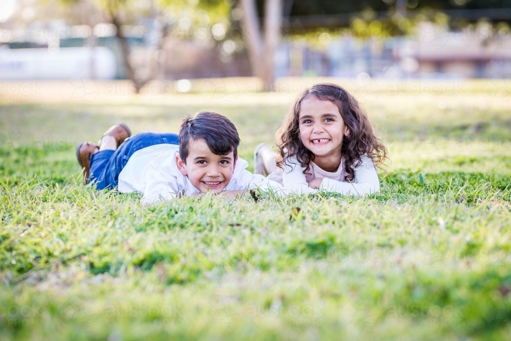 Mixed race aboriginal and caucasian twin brother and sister lying on grass smiling - Australian Stock Image