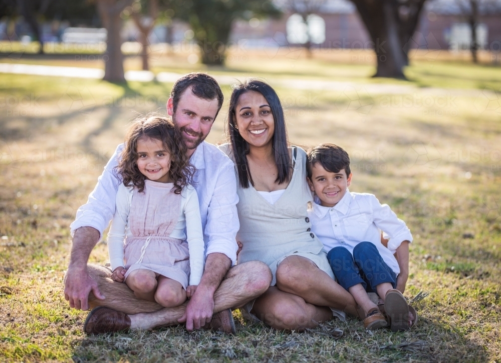 Mixed race aboriginal and caucasian twins sitting with mum and dad on grass - Australian Stock Image