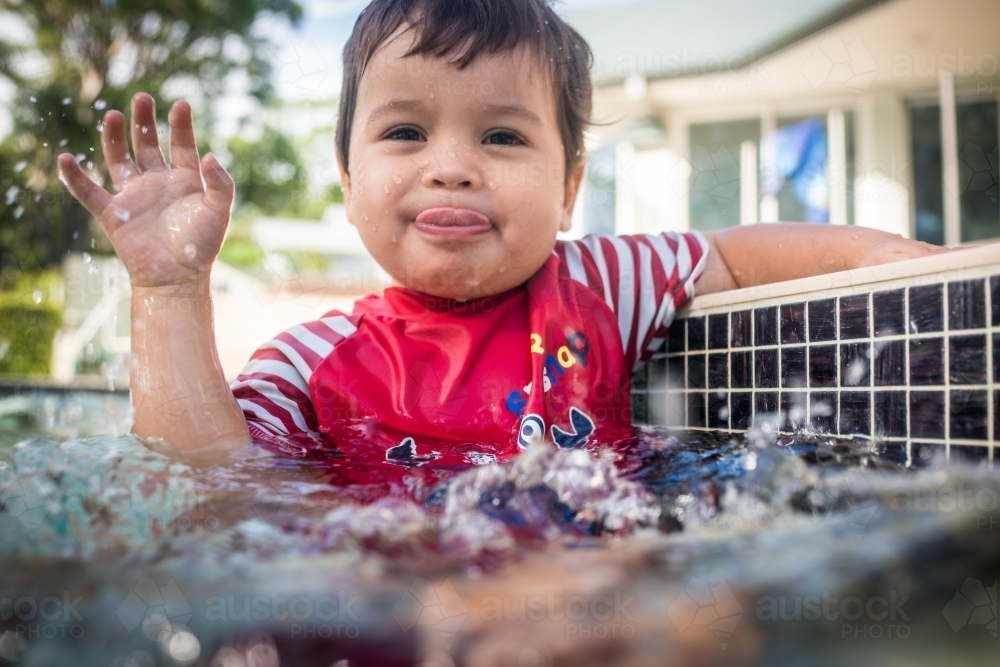 Mixed race baby boy swims and plays in a backyard pool - Australian Stock Image