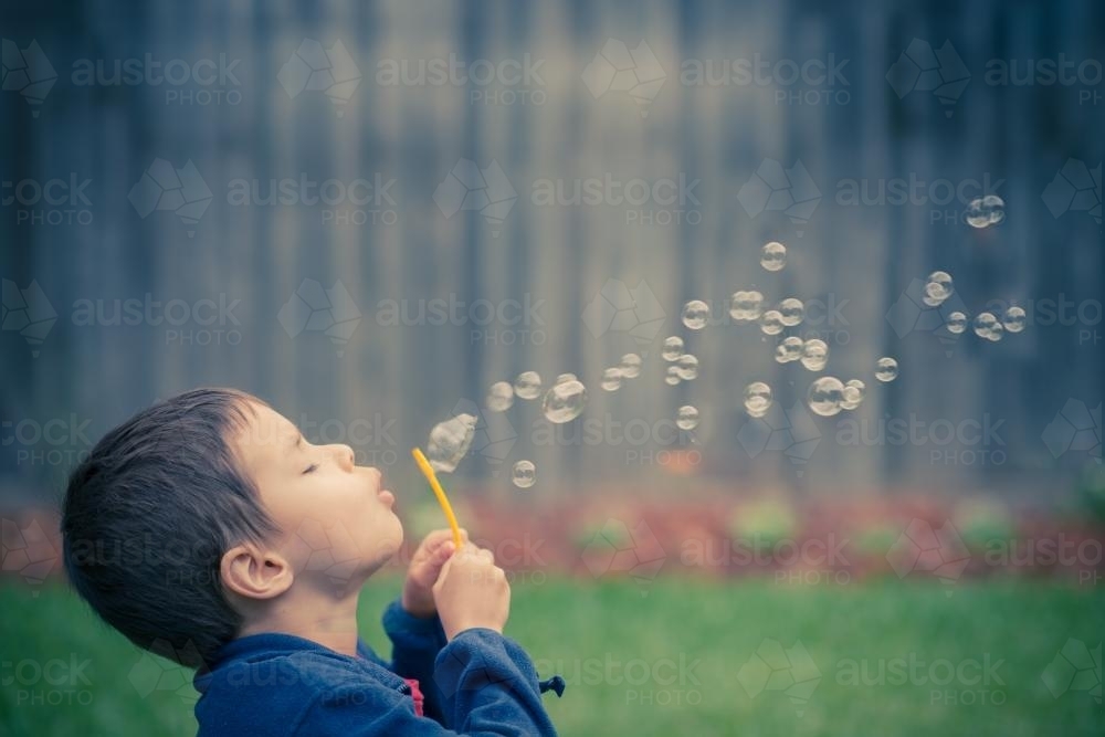 Mixed race boy blows bubbles in the yard of his suburban Sydney home - Australian Stock Image