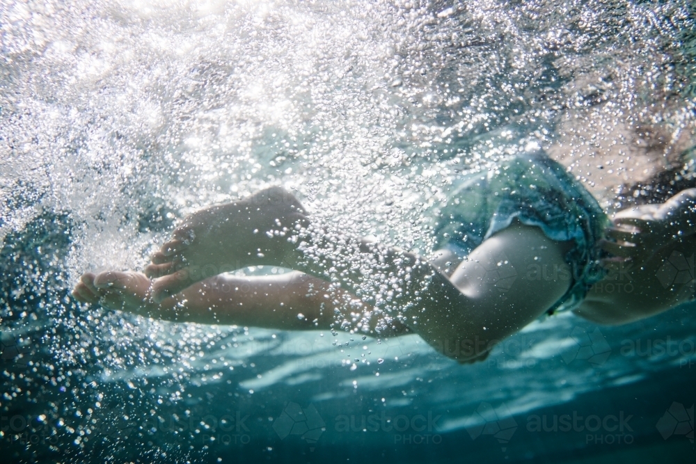 Mixed race boy swims and plays in a backyard pool - Australian Stock Image
