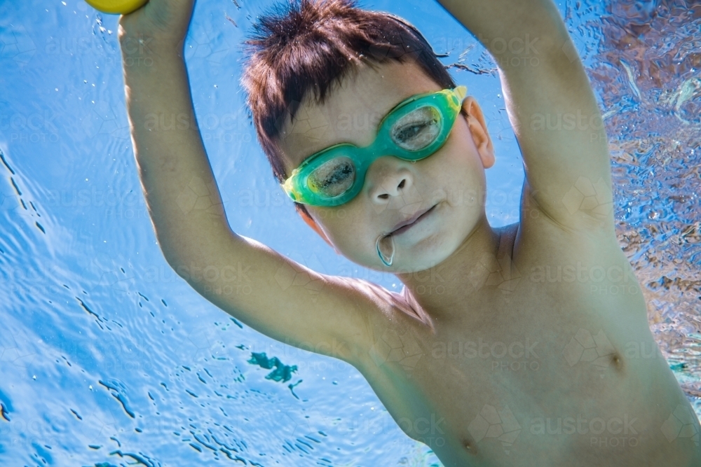 Mixed race boy swims and plays in a backyard pool - Australian Stock Image