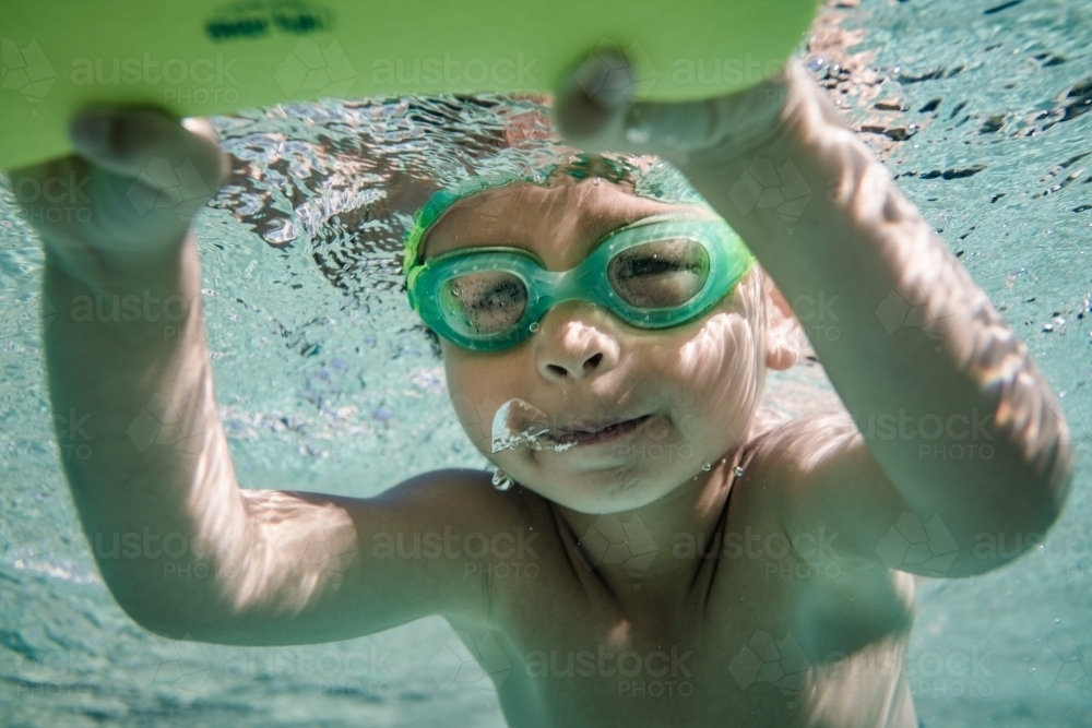 Mixed race boy swims and plays in a backyard pool - Australian Stock Image