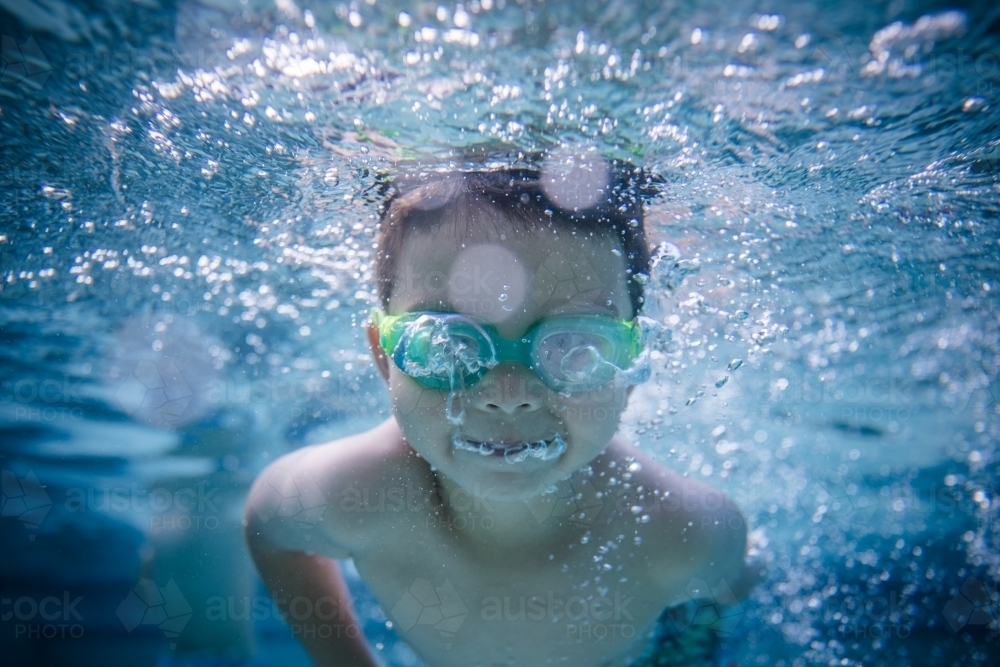 Mixed race boy swims and plays in a backyard pool - Australian Stock Image