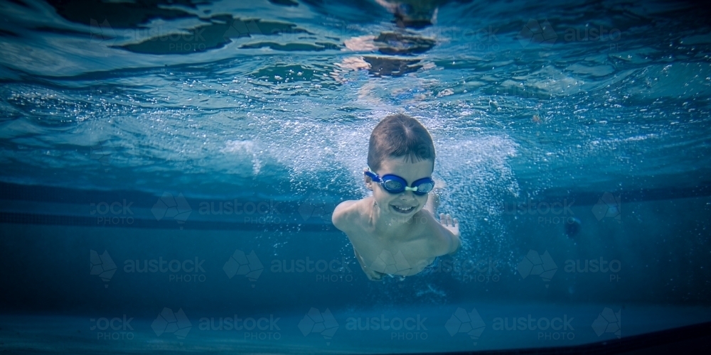 Mixed race boy swims and plays in a backyard pool - Australian Stock Image