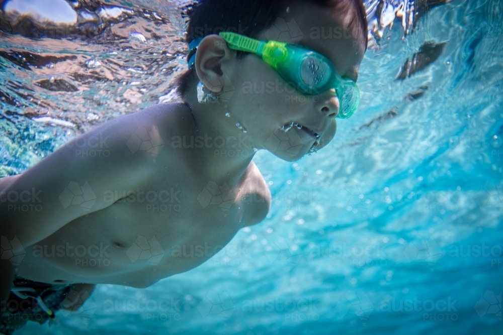 Mixed race boy swims and plays in a backyard pool - Australian Stock Image
