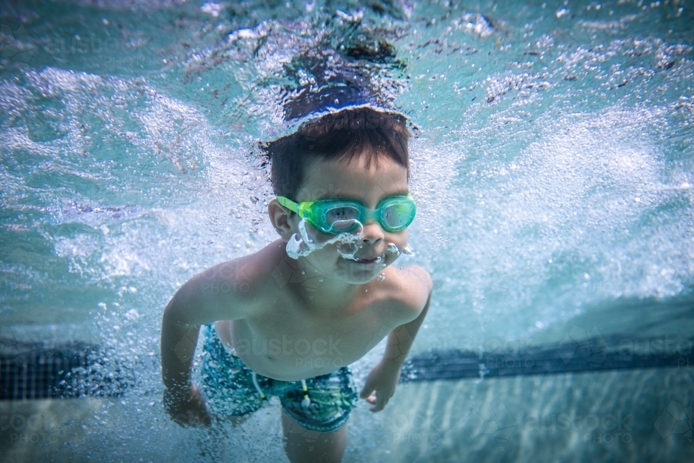 Mixed race boy swims and plays in a backyard pool - Australian Stock Image
