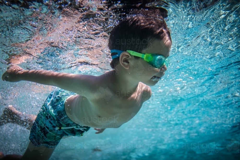Mixed race boy swims and plays in a backyard pool - Australian Stock Image
