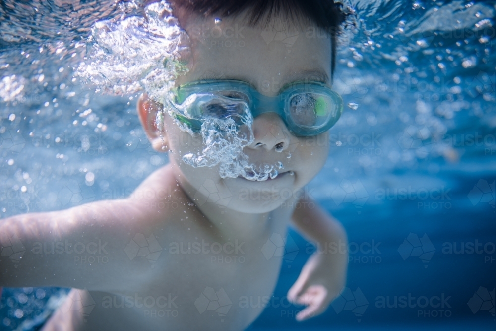 Mixed race boy swims and plays in a backyard pool - Australian Stock Image