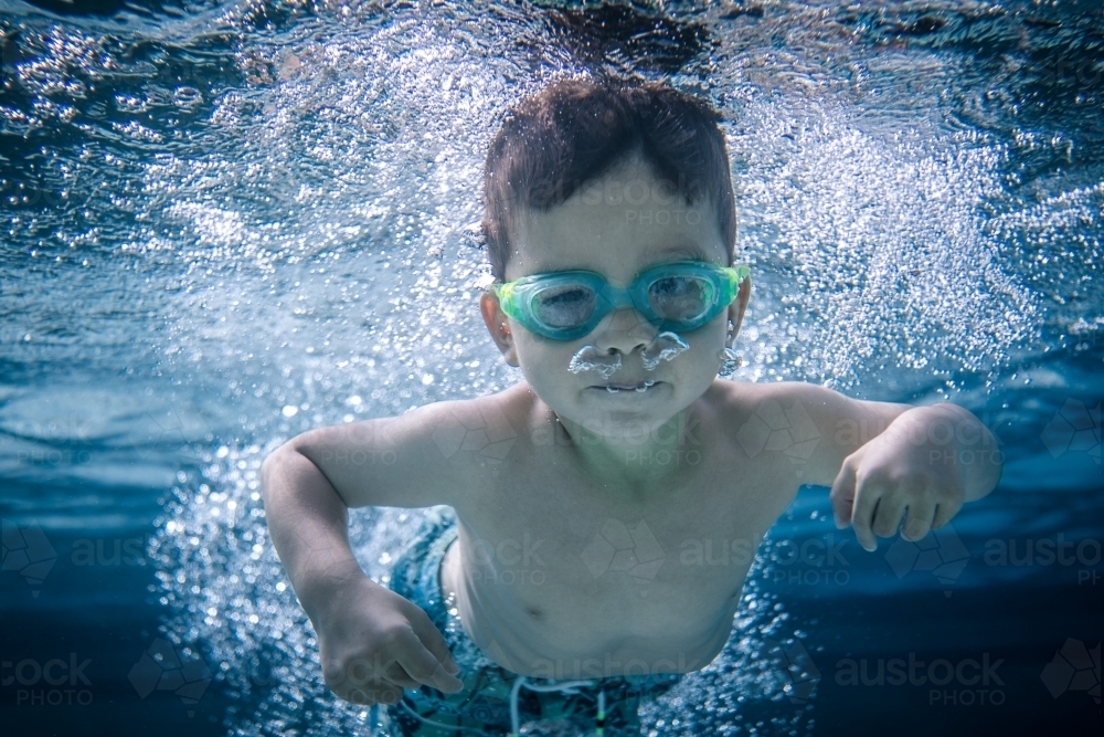 Mixed race boy swims and plays in a backyard pool - Australian Stock Image