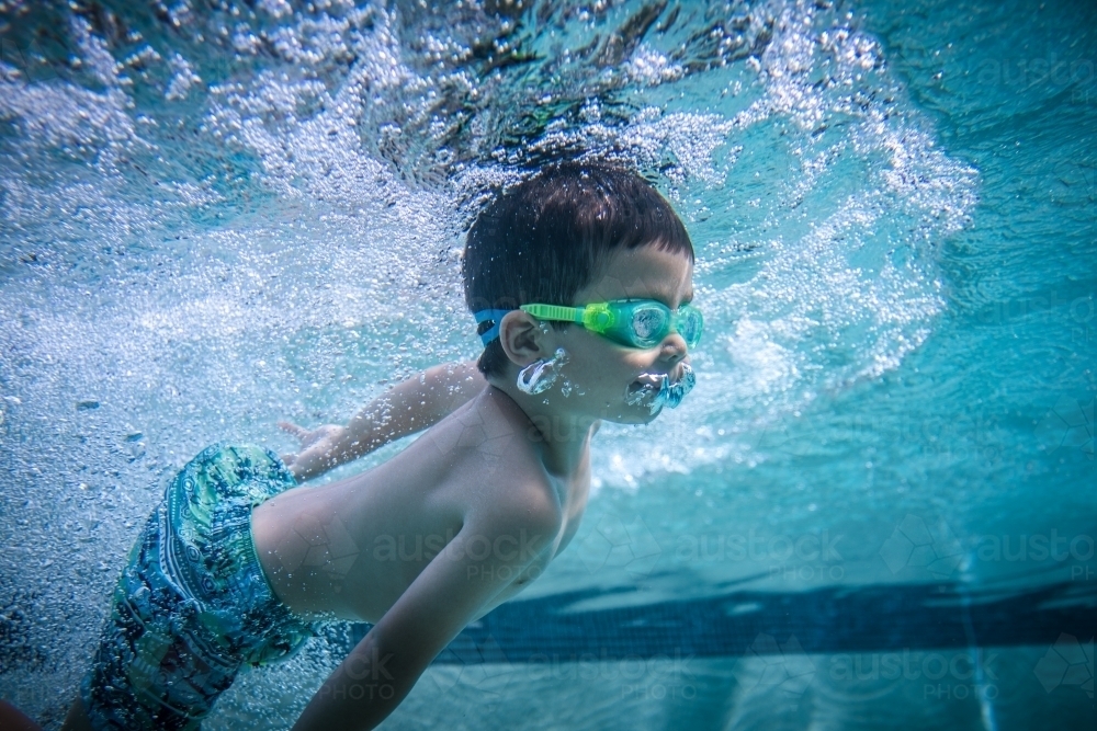 Mixed race boy swims and plays in a backyard pool - Australian Stock Image