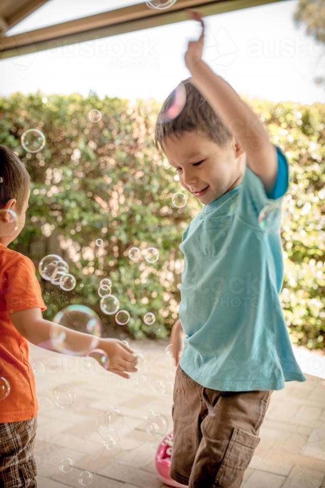 Mixed race boys play with bubbles in their suburban backyard - Australian Stock Image
