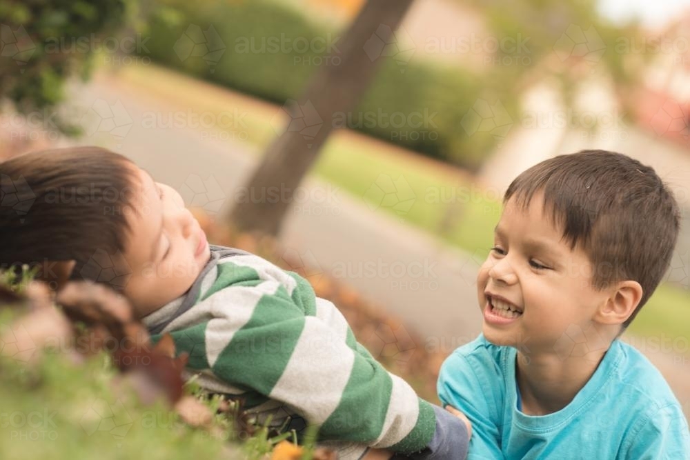 Mixed race brothers play together in the yard of their suburban Sydney home with autumn trees - Australian Stock Image