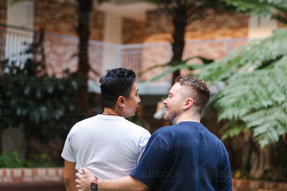 mixed race gay couple hugging - Australian Stock Image