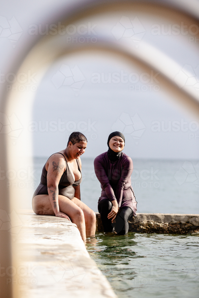 Mixed race women sitting on stone platform of the tidal pool - Australian Stock Image