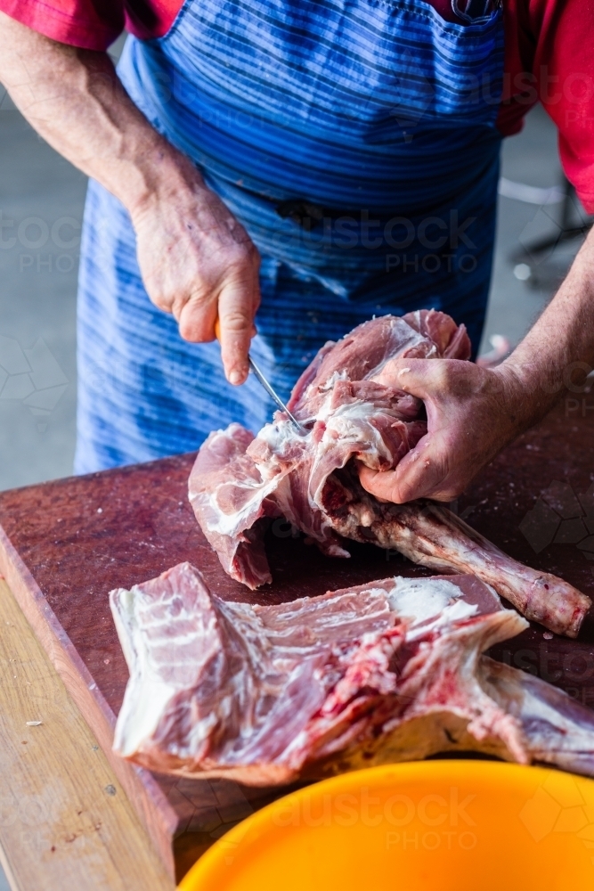 mobile butcher cutting up lamb meat, taking off the shoulder from the bone - Australian Stock Image