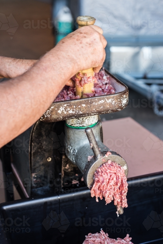 mobile butcher pushing meat through mincing machine - Australian Stock Image