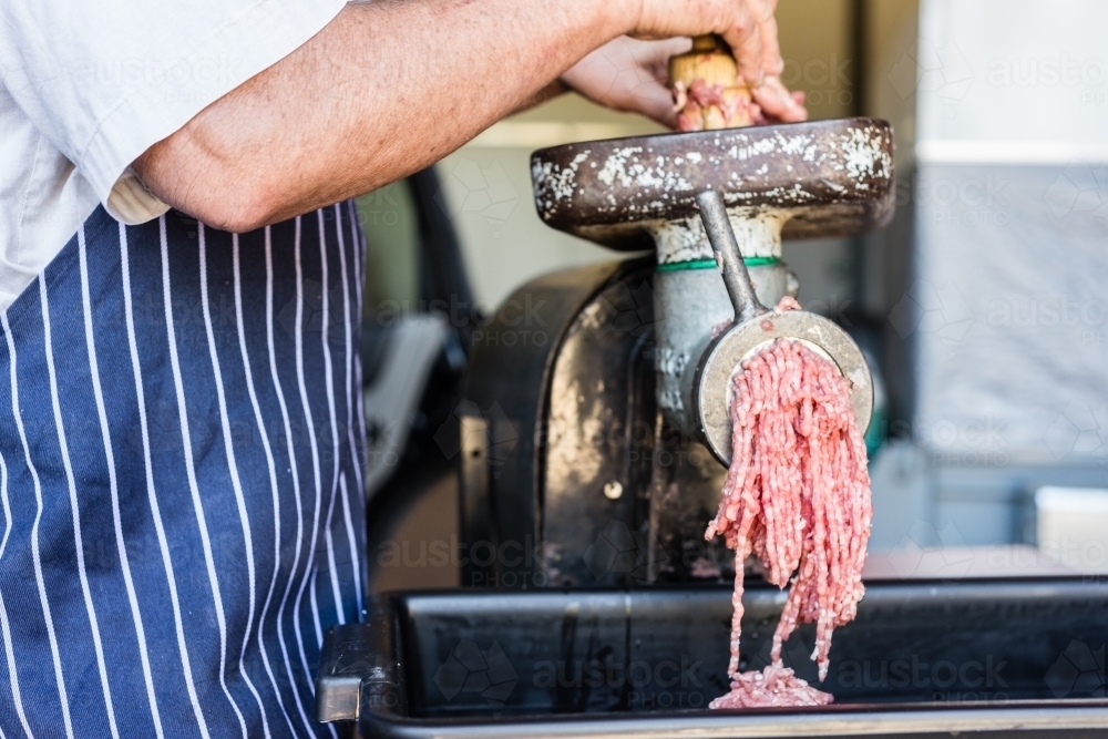 mobile butcher pushing meat through mincing machine - Australian Stock Image