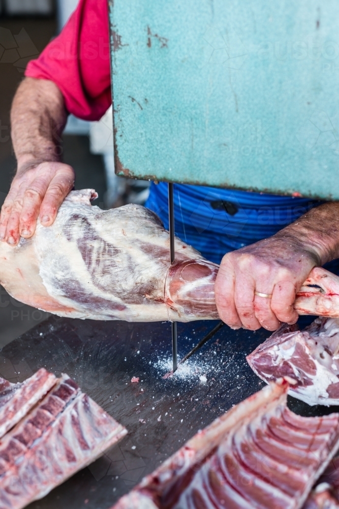 mobile butcher using electric saw to cut the shank from the leg - Australian Stock Image