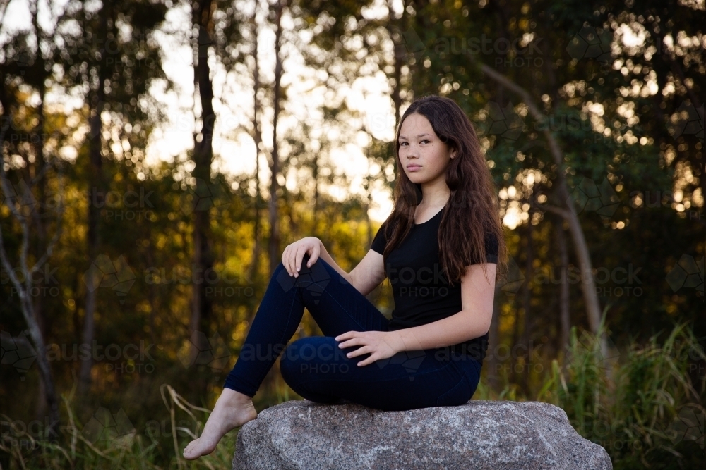 Image of Teen girl outside sitting on rock looking at camera - Austockphoto