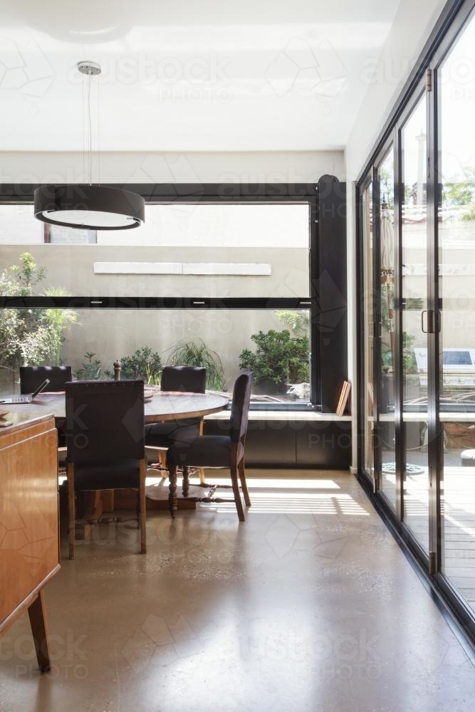 Modern dining room with concrete floor and glass bi fold doors and garden outlook - Australian Stock Image