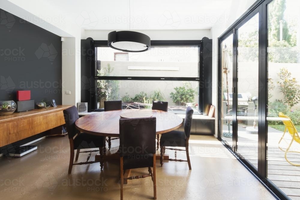 Modern dining room with concrete floor and glass bi fold doors and garden outlook - Australian Stock Image
