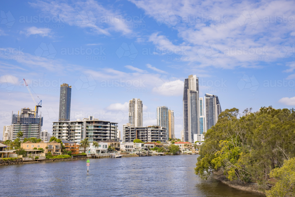 Modern high-rise buildings and waterfront residences line a wide river under a blue sky - Australian Stock Image