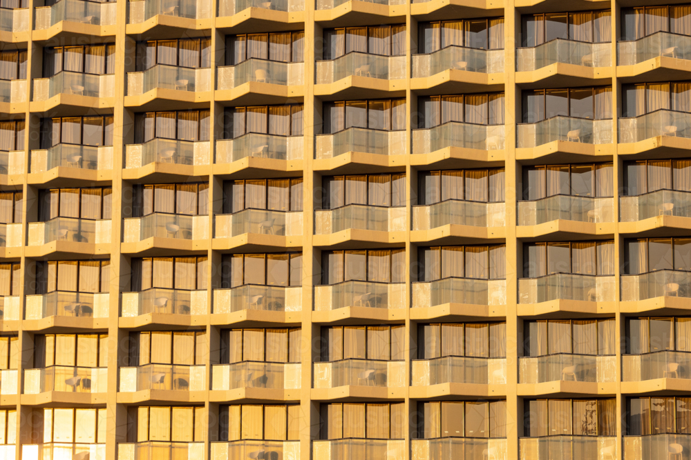 Modern hotel facade with repeating balconies and windows bathed in golden hour light - Australian Stock Image