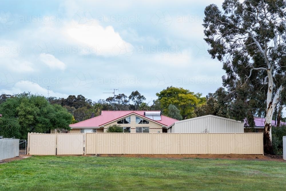 Modern house with red tin roof behind a high fence - Australian Stock Image
