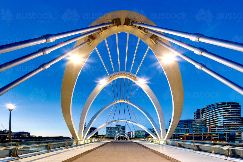 Modern pedestrian bridge framed by striking architectural arches at dusk - Australian Stock Image