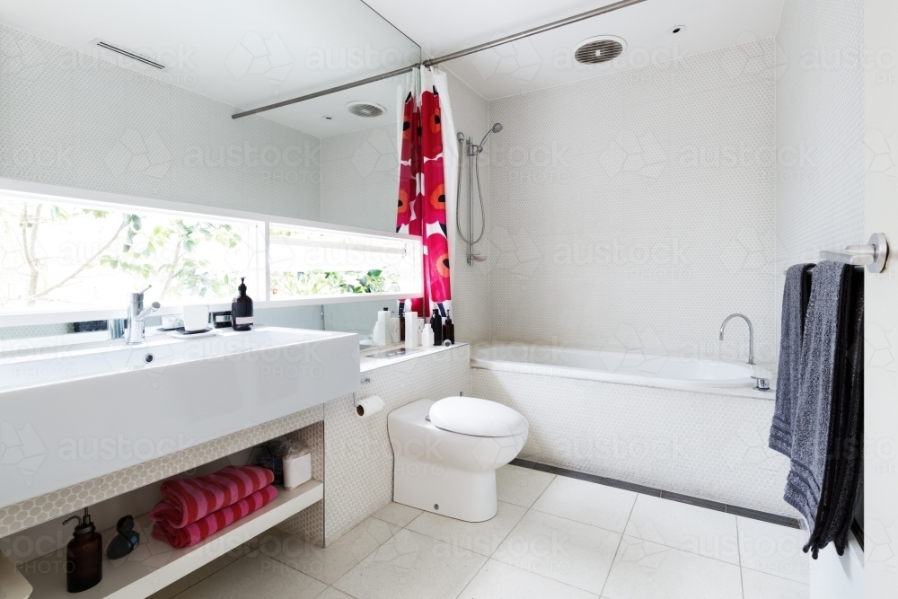 Modern renovated white mosaic tiled family bathroom with red and pink accent colors - Australian Stock Image