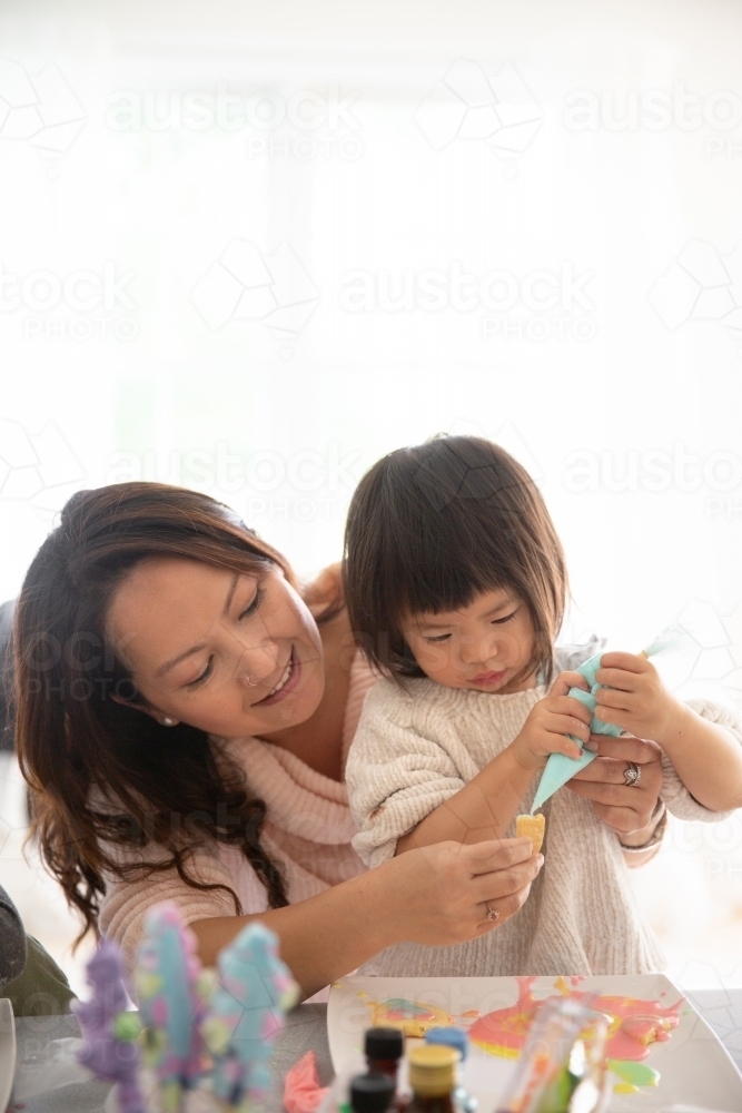 Mom and daughter doing arts and crafts making cookies at home - Australian Stock Image