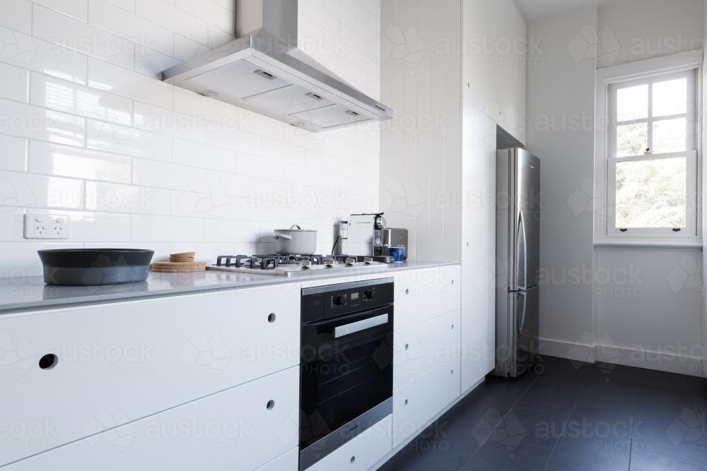 Monochrome clean white kitchen benchtop and cupboards with appliances - Australian Stock Image