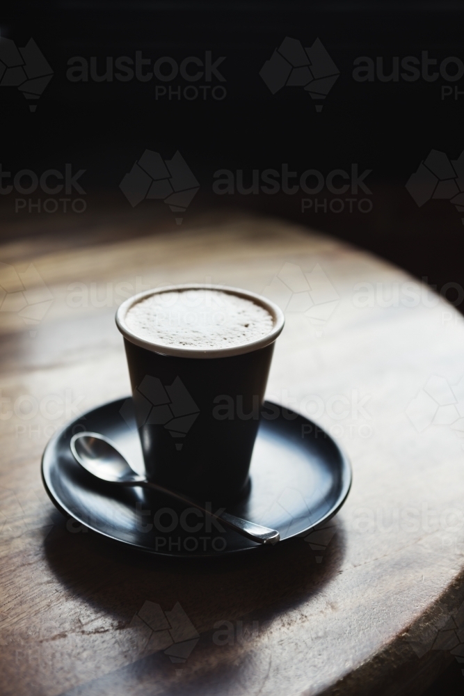 Moody restaurant setting with cafe latte by window light on rustic wooden table - Australian Stock Image