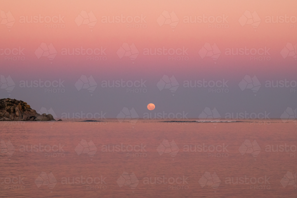 Moon going down over water with rocky island in foreground, Victor Harbor, South Australia - Australian Stock Image