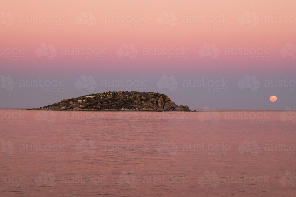Moon going down over water with rocky island in foreground, Victor Harbour, South Australia - Australian Stock Image